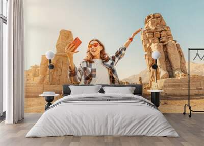 Travel blogger girl takes selfie pictures on a smartphone at the famous two Colossi of Memnon - massive ruined statues of the Pharaoh Amenhotep III. World tourism attractions Wall mural