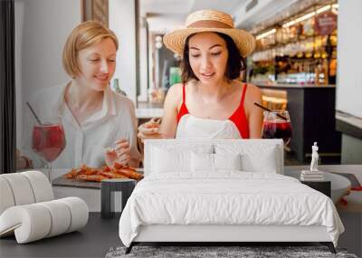 Two happy cheerful girl friends drinking wine and having lunch at seafood restaurant Wall mural