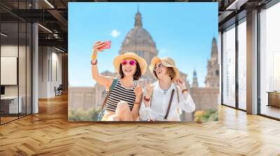 Two young happy women tourists friends hugging against the background of the National Museum of Art near the Plaza of Spain and the Montjuic Fountain in Barcelona Wall mural