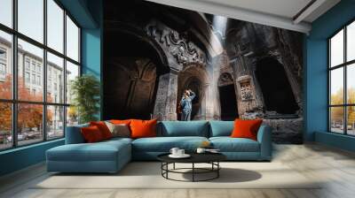 Woman tourist explores the mystical interior of the main hall of the Armenian Geghard Monastery. A ray of light falls on ancient bas-reliefs carved on the walls Wall mural