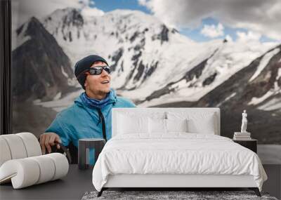 Young man mountaineer in sunglasses against blue sky and mountain glacier, adventure concept Wall mural