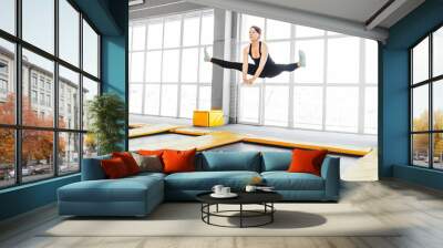 Young woman amateur acrobatic athlete jumping and exercising on a trampoline indoors, modern hobby and fitness concept Wall mural