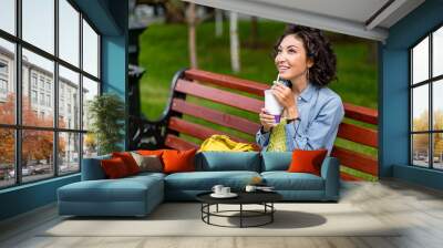 Young woman sitting on the bench with take away drink in the tra Wall mural