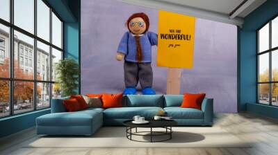 Cheerful wooden toy character presents a yellow banner featuring an inspiring quote, radiating positivity and good vibes in a charming display Wall mural