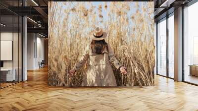 Back view of girl in trench coat and hat in tall pampas grass with blue sky on the background. Wall mural