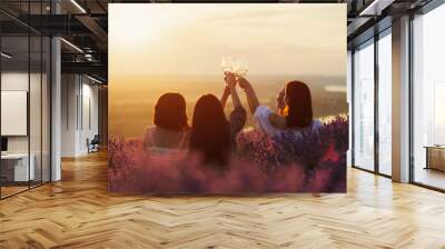 Friends having picnic in the lavender field. Group of young women sitting on lavender field at sunset on summer day. Girlfriends  drinking wine on outdoor party. Wall mural