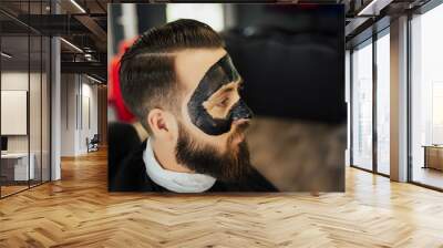 Handsome man with black charcoal face mask, concept skin care, pore cleansing from acne. Spa facial skin care for men, applying removal of black charcoal mask from nose face in barbershop. Wall mural