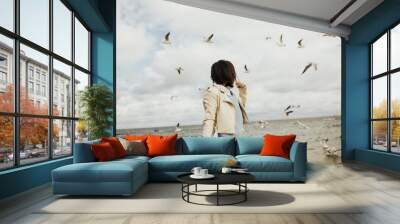 Happy young woman likes to watch at flying seagulls at sea. Seagulls fly over the water. Concept of freedom and travel. Charge of inspiration.  Lifestyle moment. Copy space. Wall mural