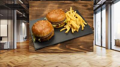 Two gourmet delicious burgers with french fries slices on a black board on a wooden background. Fast food Wall mural