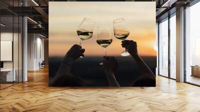 Silhouette of three glasses of white wine in female hands close-up. Celebrating an event or birthday at amazing sunset. Wall mural