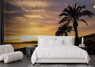 The sunset sun lights Promenade des Anglais - the main embankment of the city, one of the most beautiful in the world, and the city pebble beach. Brilliant sea beach sunset with palm trees Nice, Franc Wall mural