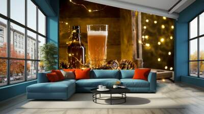 Beer in glass on wooden background with Christmas lights and pine cones Wall mural