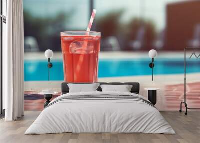 A refreshing red drink on a glass with a straw sitting on a table next to a pool Wall mural