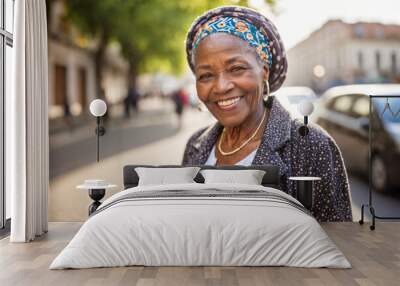 Cheerful senior black African woman with turbant smiling and using mobile phone on the street, natural sunlight with out of focus blurred background, copy space Wall mural