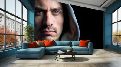 Panoramic horizontal close up portrait of young handsome hooded man with blue eyes looking at the camera with serious tranquil expression isolated on dark black background with copy space. Wall mural