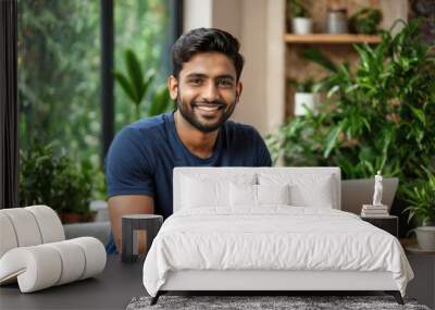 Young adult smiling Indian man looking at camera and using laptop computer at home. Young Indian entrepreneur or student, taking online class or working from home. Copy space for text Wall mural