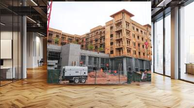 A low, angled view of an apartment complex under construction and workers installing structural steel framing  Wall mural