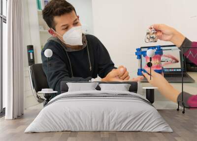 Young man with a mask receiving advice from a dentist. Wall mural