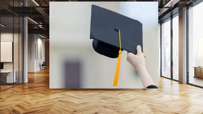 A young beautiful Asian woman university graduate in graduation gown and mortarboard holds a degree certificate stands in front of the university building after participating in college commencement Wall mural