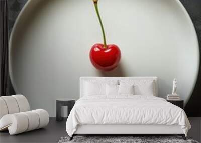 A single bright red cherry with a green stem sits on a plain white plate against a dark background Wall mural