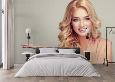 
    Blonde woman with curly hair shows your product . .Beautiful girl with beautiful smile pointing to the side . Presenting your product. Expressive facial expressions Wall mural