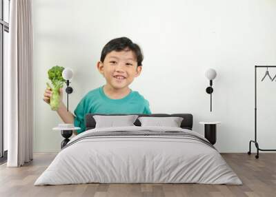 A joyful boy holds up fresh broccoli, smiling brightly against a white background. Perfect for promoting healthy eating, organic vegetables, and educational materials on healthy lifestyles. Wall mural