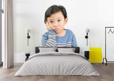 A young boy in a striped blue shirt looks bored while sitting at a table with plate of vegetables and a glass of orange juice.Perfect for themes on children's nutrition, picky eating,and healthy diets Wall mural