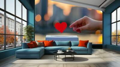 Close up of a hand putting a red heart in a white ballot box with a blurred city background Wall mural