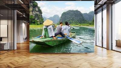 Tourists in boat. Rower using her feet to propel oars, Vietnam Wall mural