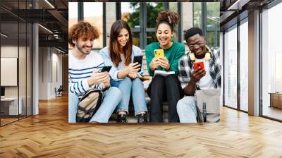 Happy University student friends having fun sharing good times on online phone app sitting on the campus staircase Wall mural