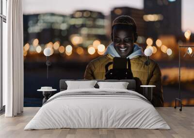 Young happy african man using cell phone in the city at night Wall mural