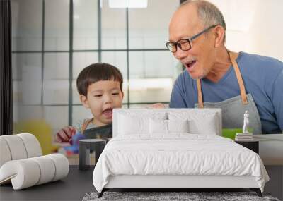 Asian Senior man and young child boy or Grandson enjoying painting together at a table, emphasizing joyful and creative family interaction indoors. Wall mural