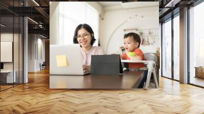 Happy smiling Asian Young mother and little son using laptop. Mom works from home office. Wall mural