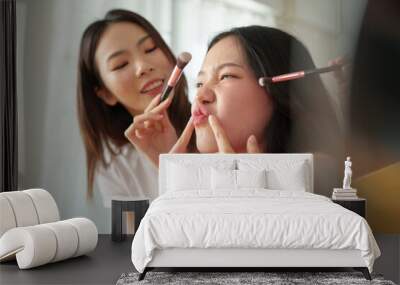 Two young Asian women playfully applying make-up, Teenage Girl smiling and making funny faces, capturing a moment of friendship and beauty. Wall mural