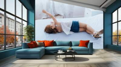 Little three years old blond girl lying on bed. Bored kid indoors Wall mural