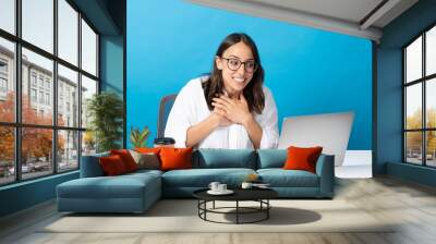 Hispanic young woman hands on heart during video call isolated on blue background. Businesswoman in front of laptop Wall mural