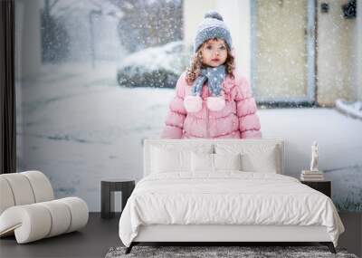 Cute baby girl in pink jacket and grey hat enjoying first snow b Wall mural