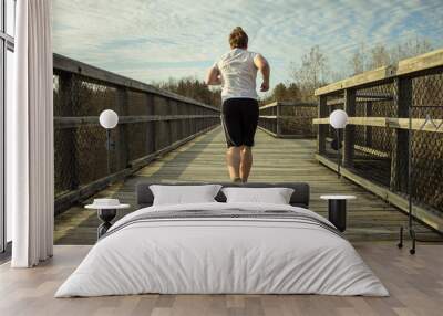 Male Jogger Running Outdoors. Young male runner in motion on wooden boardwalk outdoors. Wall mural