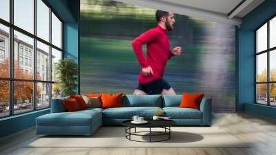 A man in a red shirt and black shorts runs through a park. The image is blurry, giving it a sense of motion and energy Wall mural