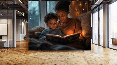 A woman and her daughter read a book together in their home at dusk, illuminated by a small lantern. Wall mural