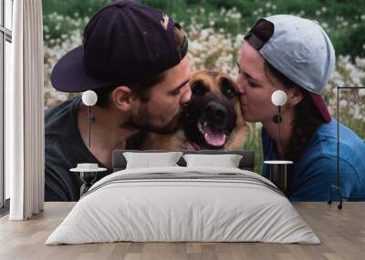 A guy and a girl kiss and hug the dog on both sides. A man, a woman, and a German shepherd. Family photo session with a dog. Wall mural