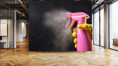 a hand in a yellow glove holds a pink spray bottle for cleaning on a black background. Concept for advertising cleaning services, web template with space for text on the left. Wall mural