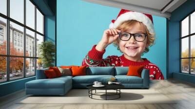 Happy little boy in santa's hat and christmas sweater holding eyeglasses, on a blue background. Christmas ophtalmologist background. christmas opthalmologyical concept. christmas medical concept Wall mural