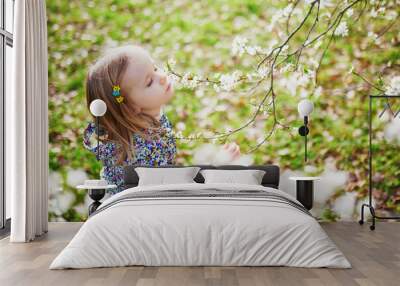 Adorable little girl enjoying nice and sunny spring day near apple tree in full bloom Wall mural