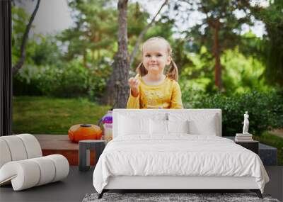 Adorable little girl sitting on the bench with lunchbox and having picnic on a summer day Wall mural