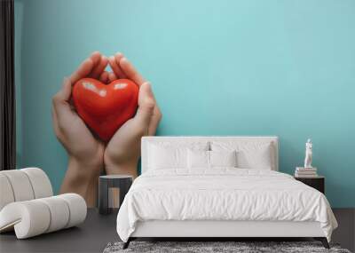 Woman hands holding red heart on solid light blue background. Health care, organ donation, cardiac health problems. Wall mural