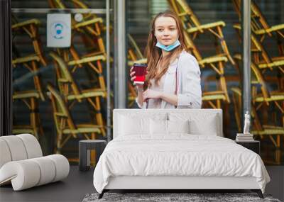 Young girl standing near closed restaurant in Paris and wearing protective face mask during coronavirus outbreak Wall mural