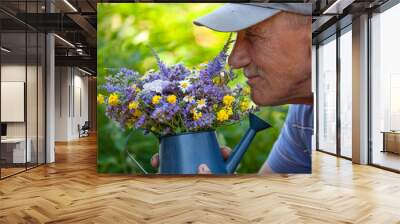 Old man smelling wild flowers in a blue metal watering can in his backyard Wall mural