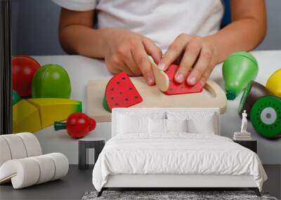 The child plays with wooden colorful toys. The child is cutting a wooden Watermelon for fruit salad. Educational logic toys for kid's. Children's hands close-up. Montessori Games for Child Development Wall mural