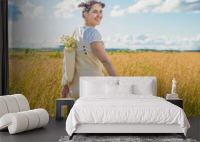 A young woman in a field. Beige clothing. Bouquet of chamomile. Wall mural